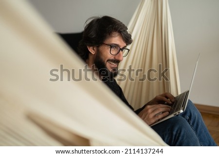 Young business man with black glasses working at home with laptop on a white hammock. Gray notebook for working. Home office concept. High quality photo