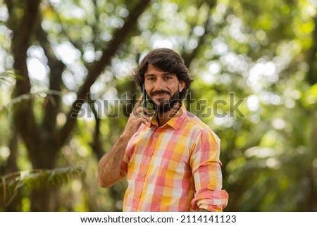 View of young man using a smartphone at day time with a green park in the background. Mobile phone, technology, urban concept. High quality photo