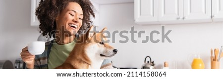 laughing african american woman holding morning coffee near shiba inu dog, banner Royalty-Free Stock Photo #2114158064