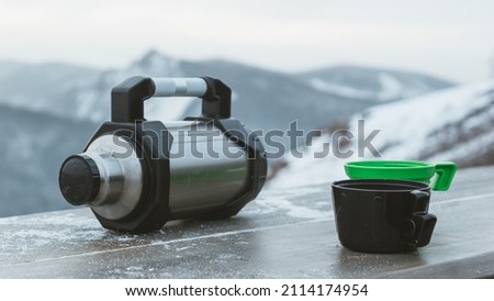 Thermos with two glasses on a wooden table on a blurred background of mountains. Snack while traveling