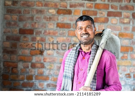 Smiling confident construction worker or labour with hose in hands turns by looking camera at workplace - concept of daily wagers lifestyle and happiness Royalty-Free Stock Photo #2114185289