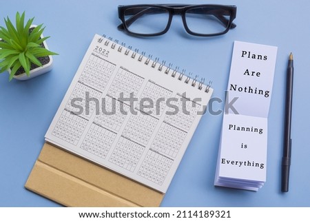 Motivational quote on notepad with 2022 calendar, glasses, pen and potted plant on a desk - Plans are nothing, planning is everything