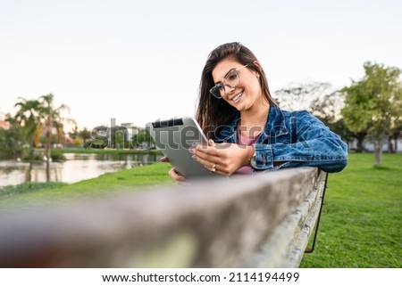 happy student reading eBook on tablet sitting in bench