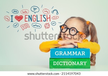 Beautiful cute little girl leaning on books, looking at the illustrations and words in English above her head. Foreign language learning concept. I love English.  Royalty-Free Stock Photo #2114197043