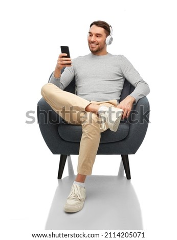 technology, people and music concept - happy smiling man with smartphone and earphones sitting in chair over white background