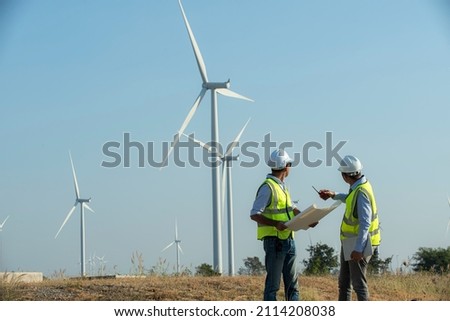 Back view of two engineers discussing against turbines on wind turbine farm. Royalty-Free Stock Photo #2114208038