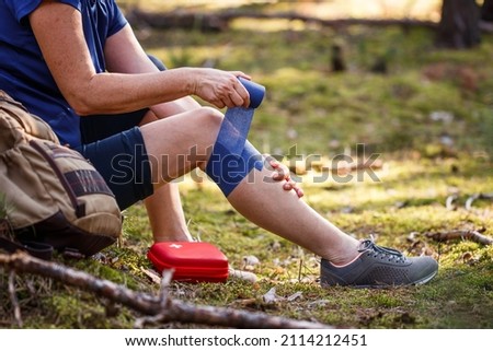 Injured hiker putting elastic bandage to her knee. Injury during hiking. First aid kit. Knee joint pain and tendon problems during adventure in nature Royalty-Free Stock Photo #2114212451