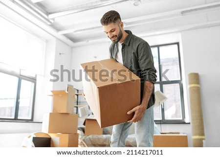 moving, people and real estate concept - happy smiling man holding boxes with stuff at new home Royalty-Free Stock Photo #2114217011