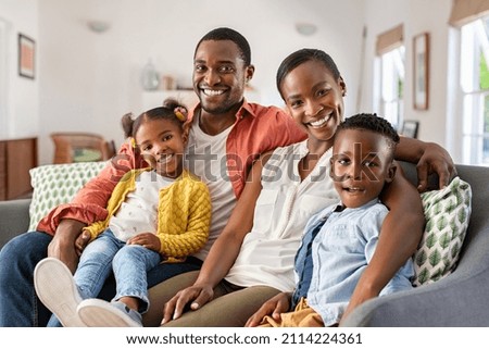 Portrait of happy mature couple with son and daughter relaxing on sofa at home. Middle aged black woman with husband and children smiling and looking at camera. Beautiful mid african american family. Royalty-Free Stock Photo #2114224361