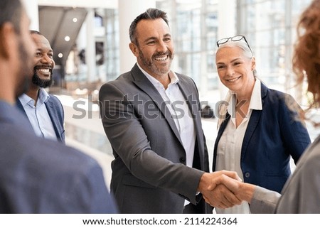 Happy mature businessman shaking hands with businesswoman in modern office. Successful entrepreneur greeting business woman with handshake. Agreement and business deal concept. Royalty-Free Stock Photo #2114224364