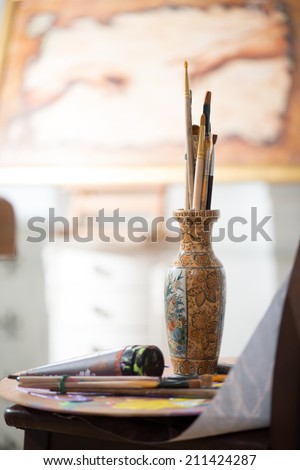 Different paintbrushes standing in one pot on the table moist colors. The picture of painter on background