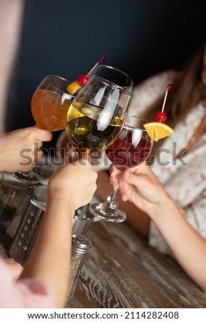 people's hands hold glasses with drinks and wine clink above the table in the restaurant