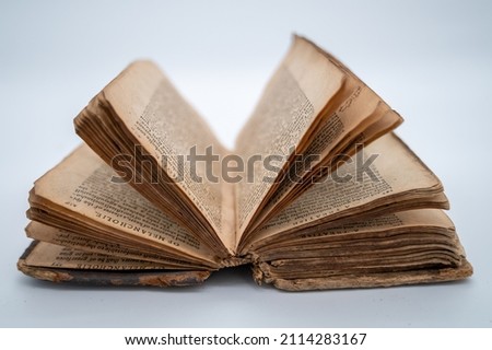 An Old Book Is Lying Flat On Both Covers Displaying A Bouquet Of Pages Opened Forming A Half Circle Within The Frame. Words are legible from the tops of the pages. Royalty-Free Stock Photo #2114283167