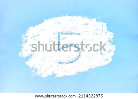 A picture of a cloud made with flour on a blue background and the number 5 drawn on it