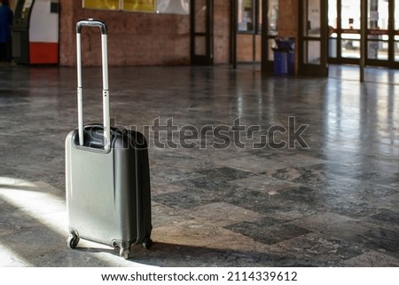 Single unattended trolley wheeled suitcase on stone floor in empty train station hall Royalty-Free Stock Photo #2114339612