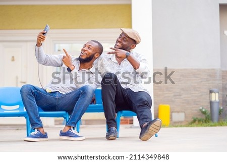 landscape image of two african guys with smart phone- excited black guys seated and enjoying social media surf.