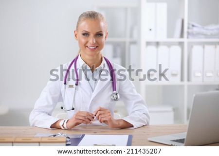 Beautiful young smiling female doctor sitting at the desk and w
