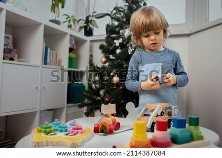Beautiful toddler play with a wooden toys at home. Toddler play with a color educational toy and wooden car.  Child play at the table in the baby room near Christmas tree.  Funny baby. Lifestyle. 