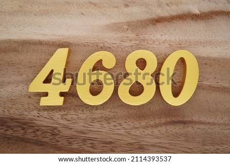 Wooden Arabic numerals 4680 painted in gold on a dark brown and white patterned plank background.