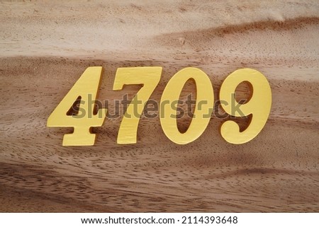 Wooden Arabic numerals 4709 painted in gold on a dark brown and white patterned plank background.