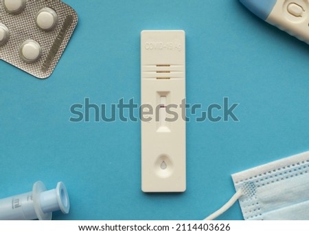 Coronavirus antigen test with a negative result on a blue bright background next to a thermometer, a medical mask, pills and a syringe