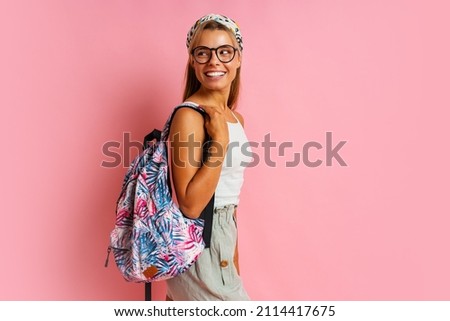 Smiling student woman  in glasses  posing on pink background. Wearing stylish summer outfit and back pack. Royalty-Free Stock Photo #2114417675