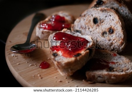 Slices of bread with raisins and strawberry jam on top, with a spoon on the side, on a wooden cutting board close up side view, food photography