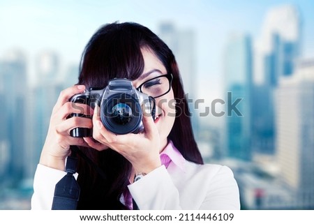 Young businesswoman using a digital camera to taking a picture while standing with modern city background