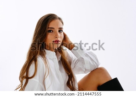 A beautiful young girl with long hair and blue eyes on a white background looks interested in the middle plan with copy space.