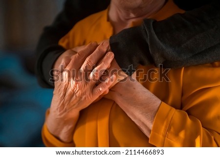 A young man, a volunteer, a son carefully hugs his beloved grandmother, supports and helps an elderly woman in retirement, his grandparent. Young male and female elderly hands with wrinkles closeup.  Royalty-Free Stock Photo #2114466893