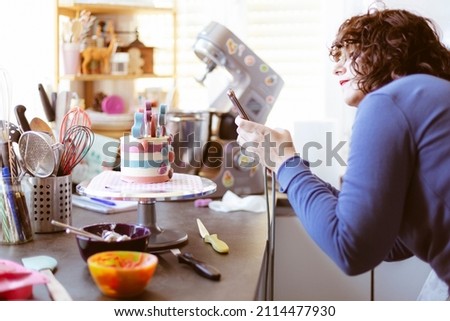Caucasian woman at home taking a picture of a cake with her mobile phone. Selective focus.