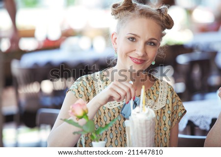Pretty cheerful young blonde woman sitting at table in coffee shop on the street