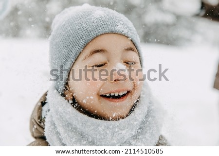 Closeup portrait of a little boy with snow on his nose, laughing, with eyes closed, on cold winter day.