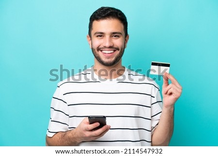 Young Brazilian man isolated on blue background buying with the mobile with a credit card Royalty-Free Stock Photo #2114547932