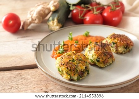Roasted vegetable balls from zucchini, potato and ginger with tomato sauce and raw ingredients on a rustic wooden table, cooking healthy and vegan, copy space, selected focus, narrow depth of field