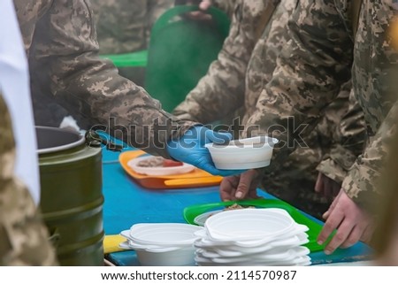 A field kitchen cook pours food for soldiers at a halt.