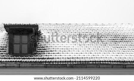 Black and white photo of traditional English house attic with snow on the roof. Attic mansard window of antique building. Copy space. Textured background.