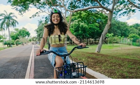 Young Latin woman in protective helmet is riding her bicycle along the bike path in a city park Royalty-Free Stock Photo #2114613698