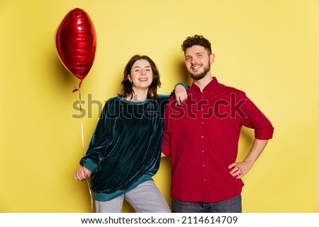 Holidays vibe. Happy couple, man and woman holding balloons shaped hearts isolated on yellow background. St. Valentine's day celebration. Concept of emotions, love, relations, romantic