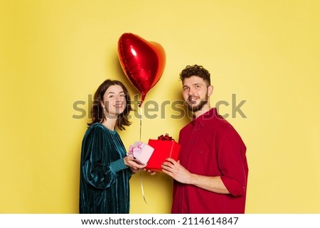 Presents. Happy couple, man and woman holding balloons shaped hearts isolated on yellow background. St. Valentine's day celebration. Concept of emotions, love, relations, romantic holidays.