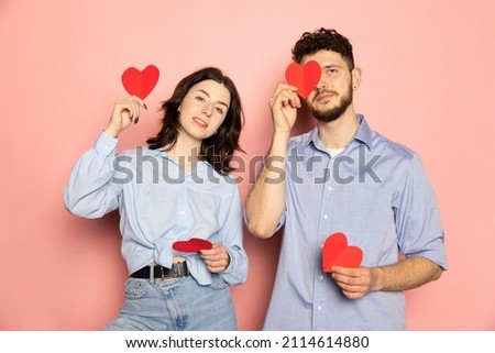 Young and happy man and woman holding greeting cards shaped hearts isolated on pink trendy color background. Human emotions, youth, love and lifestyle concept. Valentine's day celebration