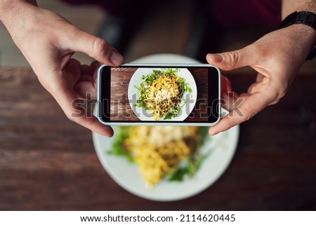 Man takes photo of spaghetti meal in restaurant using smartphone. Food photography with smartphone
