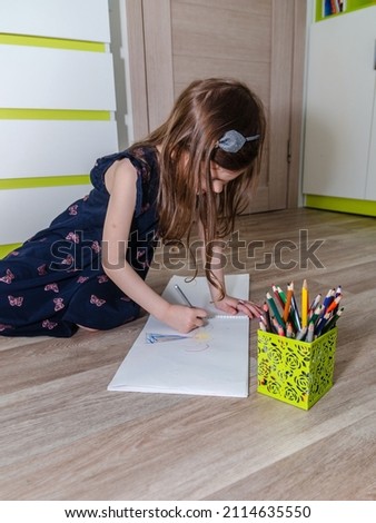 Little girl draws with pencils on the floor in her room.