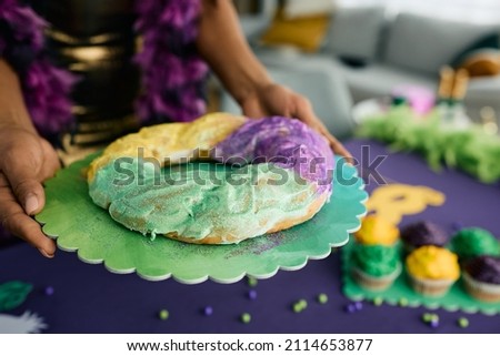 Close-up of African American woman serving Mardi Gras King cake at dining table. 