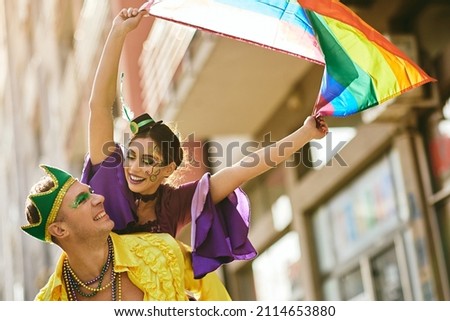 Low angle view of happy woman holding rainbow flag while man is piggybacking her during the carnival. 