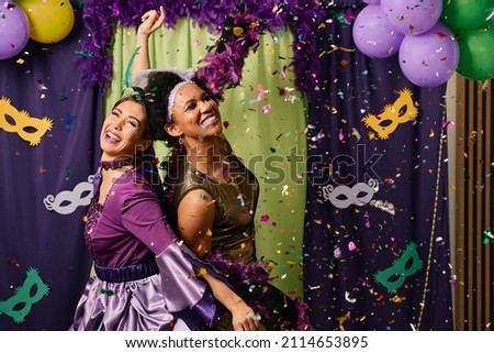 Cheerful female friends in Mardi Gras costumes dancing and having fun on carnival party. 