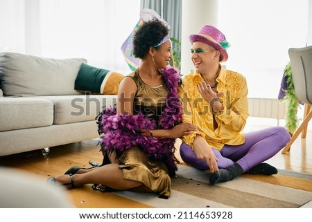 Happy African American woman and her male friend wearing Mardi Gras carnival costumes and talking at home party. 