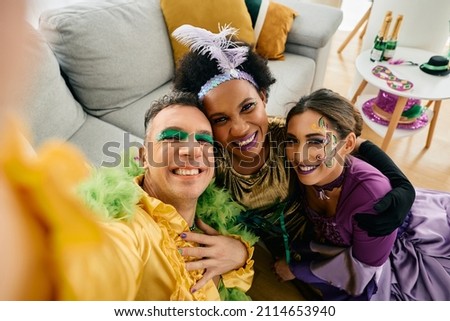 Group of happy friends in Mardi Gras costumes taking selfie while celebrating  at home party.