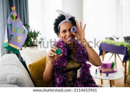 Playful African American woman having fun with food during Mardi Gras party at home. 