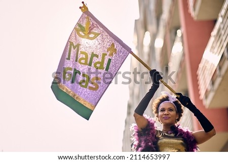 Low angle view of African American woman holding Mardi Gras flag during the carnival.